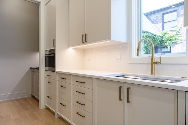 1437 Ashland Ave, River Forest, IL 60305 - kitchen featuring decorative backsplash, light wood-style flooring, light countertops, white cabinetry, and stainless steel oven
