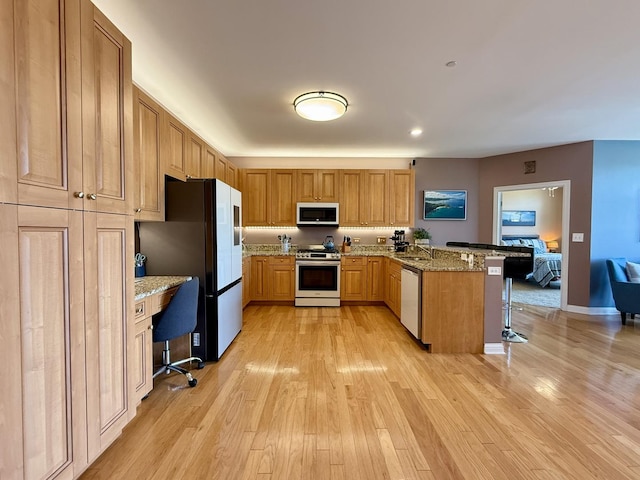 160 S River St Unit 204, Aurora, IL 60506 - kitchen with appliances with stainless steel finishes, a kitchen breakfast bar, a peninsula, light wood finished floors, and light stone counters