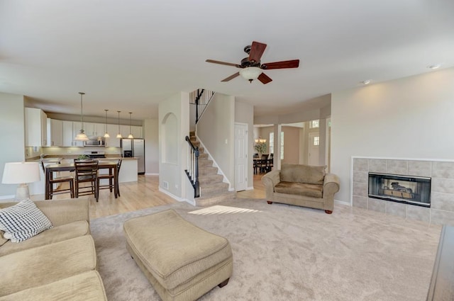 11703 Wolf Creek Ln, Plainfield, IL 60585 - living room featuring a ceiling fan, stairway, a tile fireplace, and light wood-style floors