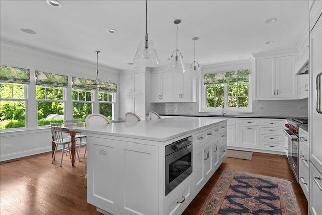 1111 Seneca Rd, Wilmette, IL 60091 - kitchen featuring stainless steel appliances, backsplash, an island with sink, white cabinetry, and crown molding