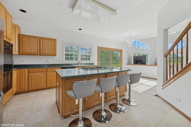 1456 Della Dr, Hoffman Estates, IL 60169 - kitchen with a kitchen bar, a kitchen island, stainless steel gas stovetop, dark stone counters, and a sink