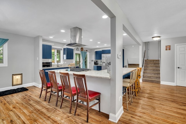1810 Jana Ln, Morris, IL 60450 - kitchen with island exhaust hood, blue cabinets, stainless steel appliances, a kitchen breakfast bar, and light wood finished floors