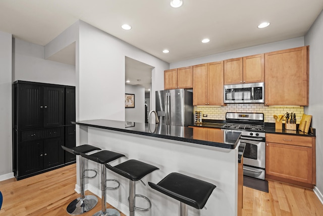 3021 W Armitage Ave Unit 201, Chicago, IL 60647 - kitchen featuring appliances with stainless steel finishes, dark countertops, light wood-type flooring, a kitchen bar, and backsplash