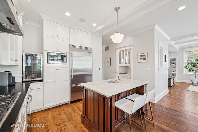 625 Park Ave, Wilmette, IL 60091 - kitchen featuring built in appliances, extractor fan, ornamental molding, wood finished floors, and a kitchen breakfast bar