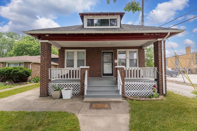 bungalow-style home with a porch, brick siding, and roof with shingles