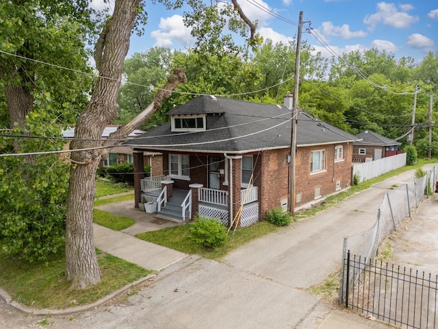 bungalow-style home with covered porch, brick siding, a shingled roof, and a chimney