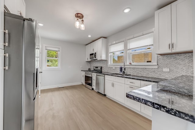 kitchen with stainless steel appliances, light wood finished floors, white cabinetry, decorative backsplash, and dark stone countertops
