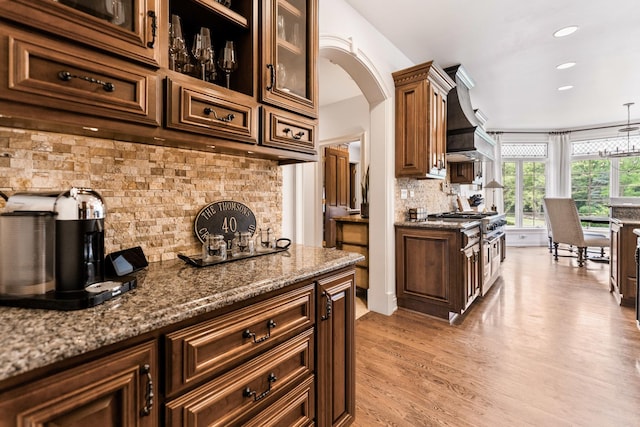 7N230 Sims Ln, Saint Charles, IL 60175 - kitchen featuring backsplash, stone countertops, custom exhaust hood, light wood-type flooring, and arched walkways
