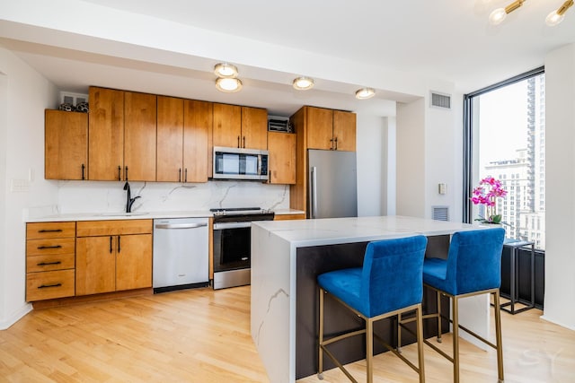 100 E Walton St Unit 38H, Chicago, IL 60611 - kitchen with stainless steel appliances, light wood-style floors, brown cabinets, tasteful backsplash, and a kitchen bar