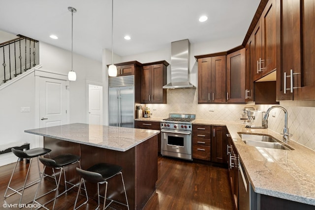 639 W Briar Pl Unit 4W, Chicago, IL 60657 - kitchen featuring high end appliances, wall chimney exhaust hood, dark wood-style floors, a breakfast bar area, and light stone countertops
