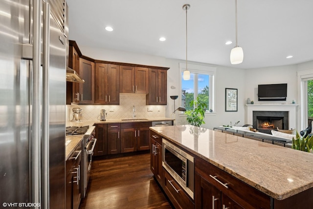 639 W Briar Pl Unit 4W, Chicago, IL 60657 - kitchen featuring premium appliances, decorative backsplash, dark wood-type flooring, a warm lit fireplace, and light stone countertops