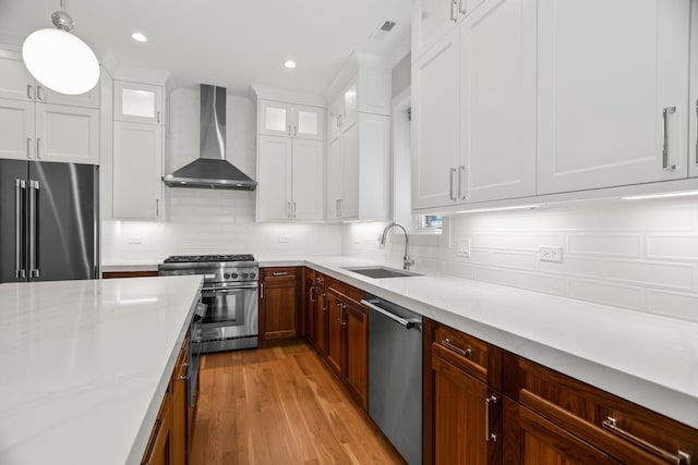 4133 N Kenmore Ave Unit 2S, Chicago, IL 60613 - kitchen featuring wall chimney range hood, high quality appliances, light wood-style flooring, backsplash, and white cabinetry