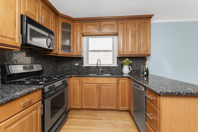 4567 N Merrimac Ave, Chicago, IL 60630 - kitchen featuring appliances with stainless steel finishes, a peninsula, light wood-style floors, dark stone counters, and brown cabinetry