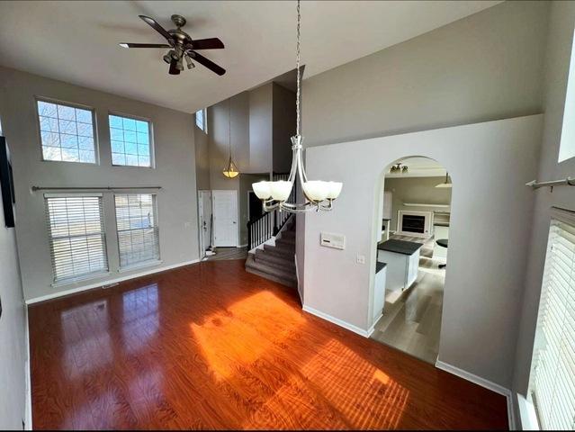 1214 Vista Dr, Gurnee, IL 60031 - unfurnished living room with a ceiling fan, a fireplace, a towering ceiling, arched walkways, and wood finished floors