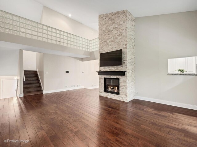 2S578 Patrick Henry Sq Unit 578, Oak Brook, IL 60523 - unfurnished living room featuring a towering ceiling, hardwood / wood-style floors, a stone fireplace, and stairs