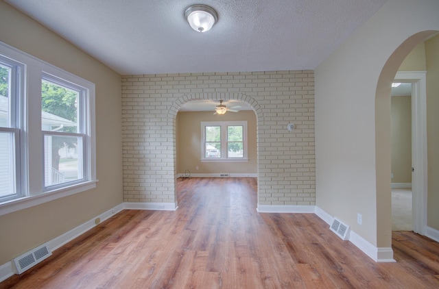 1318 N Prairie Ave, Joliet, IL 60435 - empty room with arched walkways, wood finished floors, a textured ceiling, ceiling fan, and brick wall