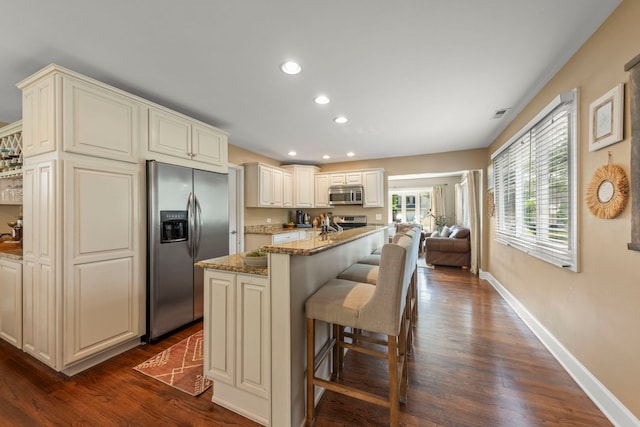1341 S Sumner St, Wheaton, IL 60189 - kitchen featuring appliances with stainless steel finishes, light stone counters, cream cabinets, dark wood-type flooring, and a kitchen island with sink