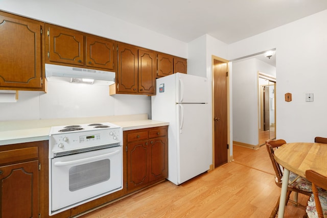kitchen with under cabinet range hood, white appliances, light wood-style flooring, light countertops, and brown cabinets