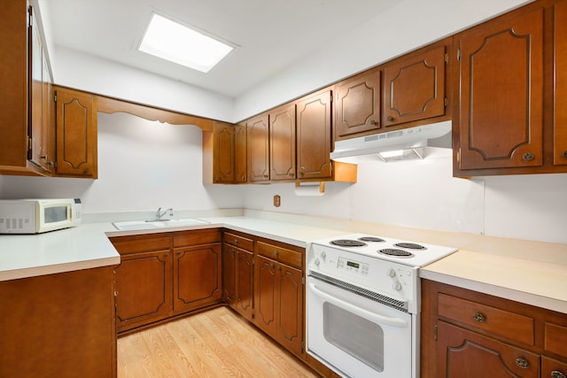 kitchen featuring white appliances, under cabinet range hood, light wood-style flooring, light countertops, and brown cabinets