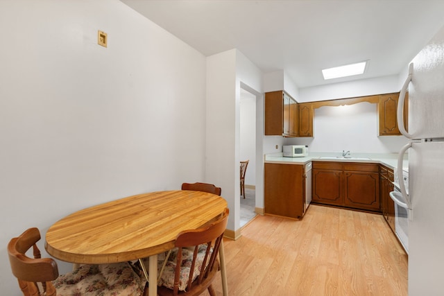 kitchen with white appliances, brown cabinetry, light wood finished floors, and light countertops