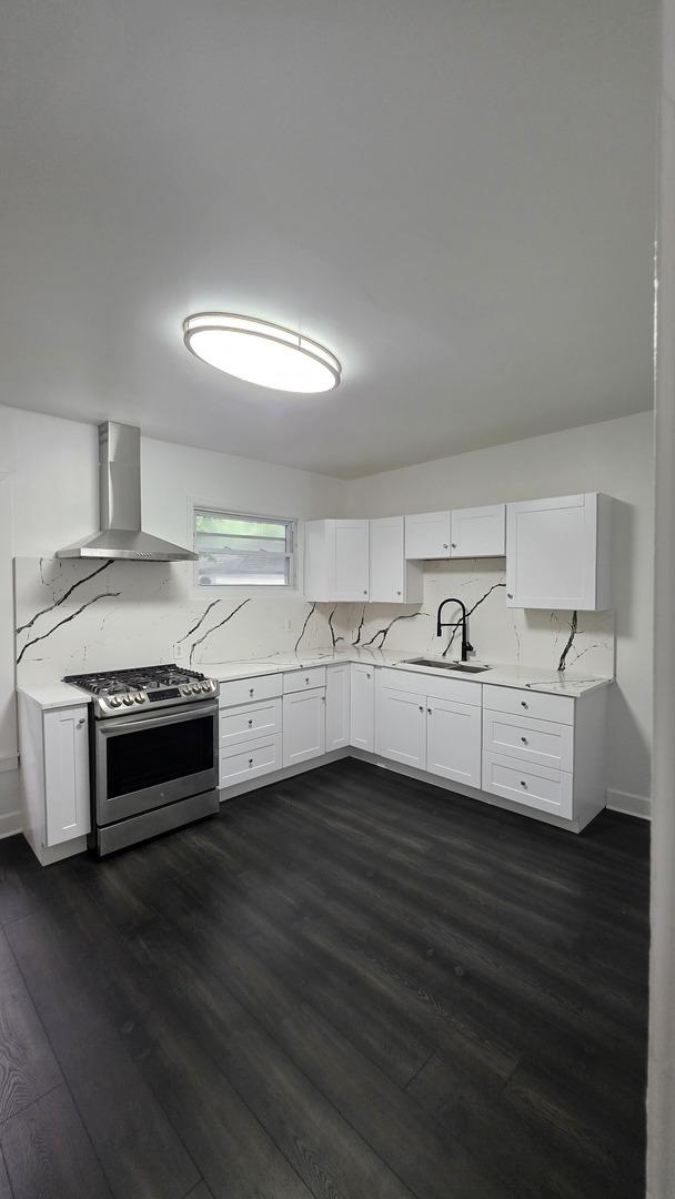 208 N Chestnut St, Aurora, IL 60506 - kitchen with wall chimney range hood, stainless steel gas stove, dark wood finished floors, and white cabinetry