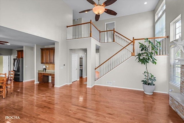 13311 Morning Mist Pl, Plainfield, IL 60585 - unfurnished living room with ceiling fan, a high ceiling, light wood-style flooring, stairs, and plenty of natural light
