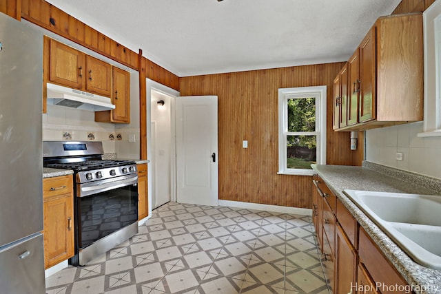 1504 W Monroe St, Waukegan, IL 60085 - kitchen with under cabinet range hood, stainless steel appliances, light flooring, wood walls, and brown cabinetry
