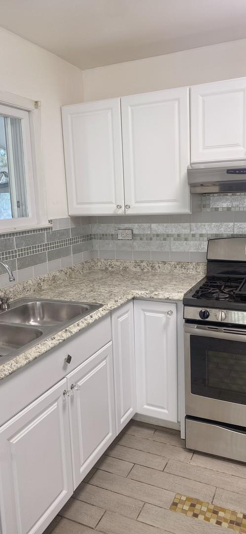 396 Thelma Ct, Wheeling, IL 60090 - kitchen featuring stainless steel range with gas stovetop, custom exhaust hood, backsplash, and white cabinetry