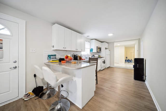 3348 N Narragansett Ave, Chicago, IL 60634 - kitchen with white appliances, a kitchen breakfast bar, light wood-style floors, white cabinetry, and tasteful backsplash