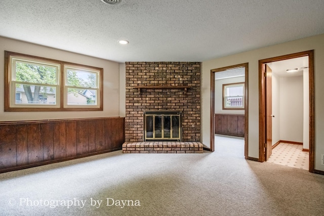 1033 Pheasant Dr, Bradley, IL 60915 - unfurnished living room featuring a textured ceiling, carpet flooring, a brick fireplace, wooden walls, and wainscoting