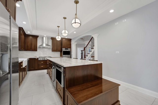 445 E Crescent Ave, Elmhurst, IL 60126 - kitchen featuring appliances with stainless steel finishes, wall chimney exhaust hood, decorative columns, a tray ceiling, and a kitchen island