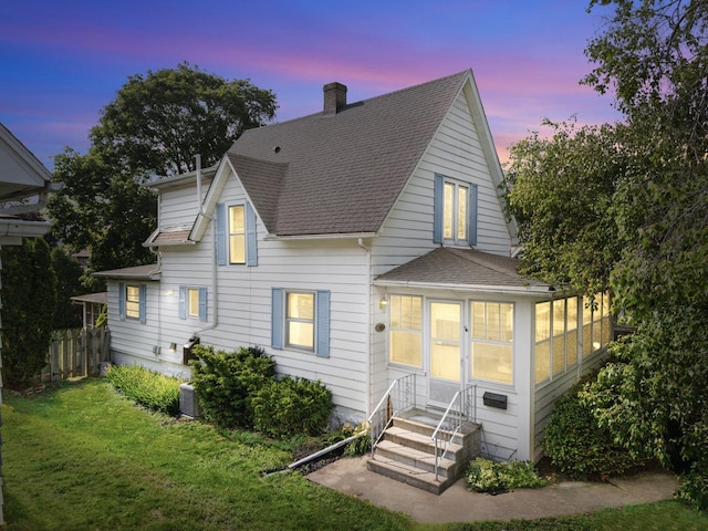 715 N 4th St, Dekalb, IL 60115 - back of house at dusk with a shingled roof, a chimney, entry steps, and a sunroom