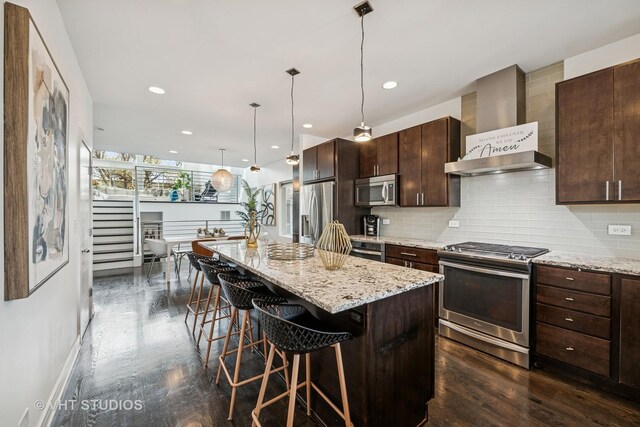 2503 N Maplewood Ave, Chicago, IL 60647 - kitchen featuring stainless steel appliances, wall chimney exhaust hood, a breakfast bar area, a kitchen island, and decorative backsplash