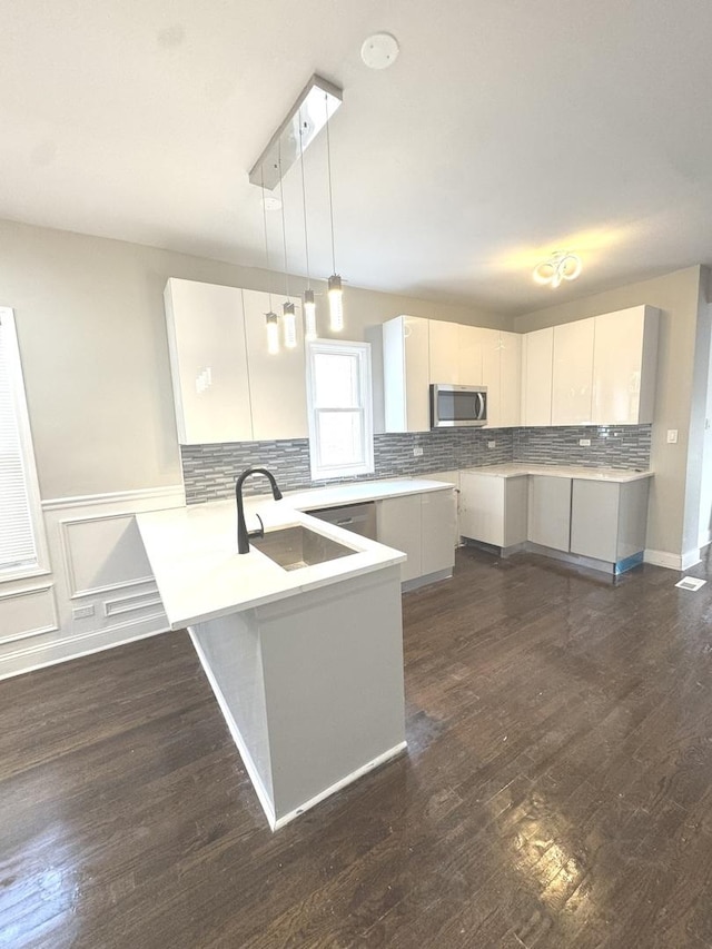9432 S Vernon Ave, Chicago, IL 60619 - kitchen featuring stainless steel microwave, a peninsula, hanging light fixtures, tasteful backsplash, and dark wood-style floors