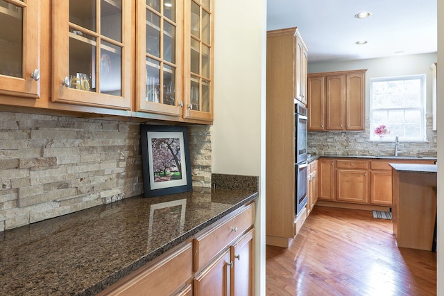606 Ebony Dr, Oswego, IL 60543 - kitchen featuring light wood-type flooring, dark stone countertops, decorative backsplash, glass insert cabinets, and recessed lighting
