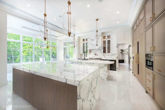 219 Lincoln Dr, Glencoe, IL 60022 - kitchen featuring a large island with sink, hanging light fixtures, decorative backsplash, light stone counters, and glass insert cabinets