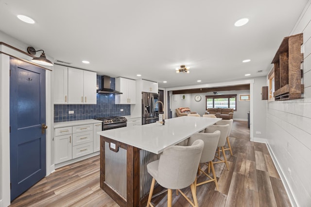 16430 S 89th Ave, Orland Park, IL 60462 - kitchen featuring wall chimney range hood, appliances with stainless steel finishes, a breakfast bar, light countertops, and a kitchen island with sink