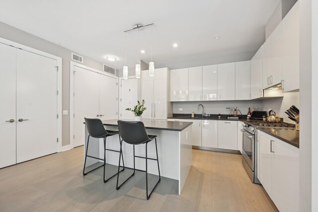 1701 W Webster Ave Unit 512, Chicago, IL 60614 - kitchen featuring stainless steel range with gas stovetop, dark countertops, light wood finished floors, white cabinets, and a breakfast bar