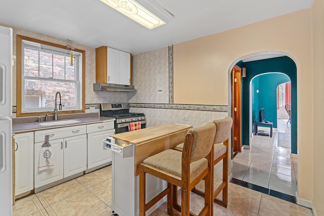3609 S Leavitt St, Chicago, IL 60609 - kitchen with under cabinet range hood, stainless steel gas range, light tile patterned floors, arched walkways, and tile walls