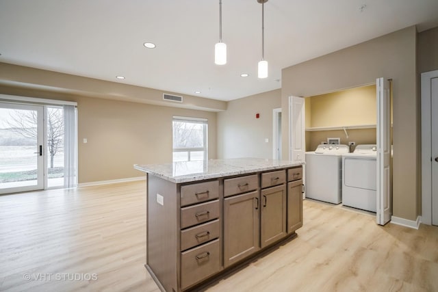 2150 Founders Dr Unit P109, Northbrook, IL 60062 - kitchen featuring separate washer and dryer, light wood finished floors, a kitchen island, hanging light fixtures, and light stone counters