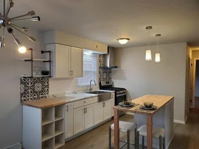 605 Hoxie Ave, Calumet City, IL 60409 - kitchen with wall chimney range hood, gas stove, dark wood-style flooring, white cabinets, and open shelves