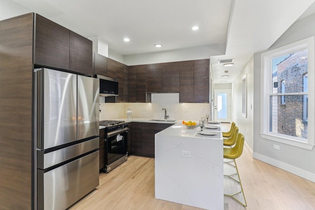 2307 N Avers Ave Unit 2, Chicago, IL 60647 - kitchen featuring appliances with stainless steel finishes, light wood finished floors, dark brown cabinetry, a kitchen breakfast bar, and recessed lighting