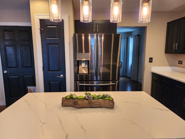 723 Casey Dr, Minooka, IL 60447 - kitchen featuring stainless steel refrigerator with ice dispenser, dark cabinetry, hanging light fixtures, and light stone countertops