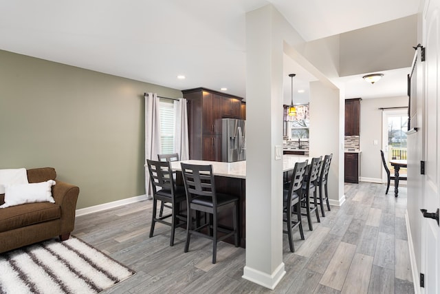1792 Autumn Woods Ln, Romeoville, IL 60446 - kitchen with stainless steel fridge with ice dispenser, a breakfast bar area, dark brown cabinetry, light wood-type flooring, and light stone counters