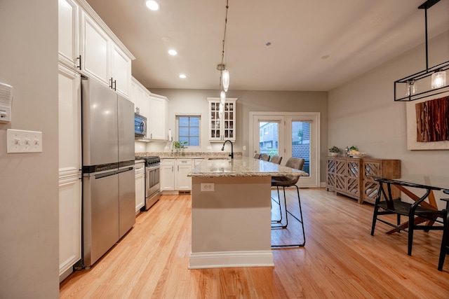 3457 N Whipple St, Chicago, IL 60618 - kitchen featuring appliances with stainless steel finishes, light wood-style floors, a breakfast bar, an island with sink, and white cabinetry