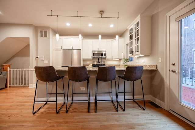 3457 N Whipple St, Chicago, IL 60618 - kitchen featuring appliances with stainless steel finishes, glass insert cabinets, a kitchen bar, light stone countertops, and recessed lighting