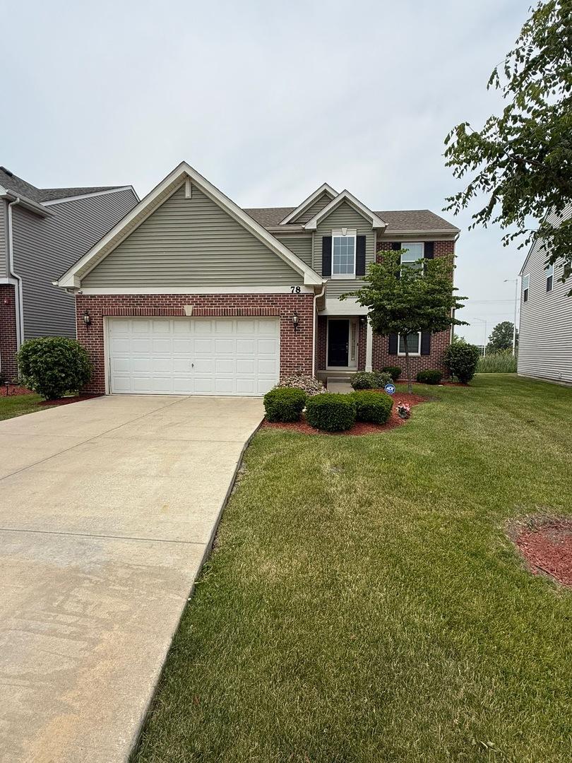 traditional-style house with brick siding, an attached garage, concrete driveway, and a front yard