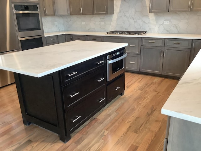 12415 Foxborough Dr, Mokena, IL 60448 - kitchen with appliances with stainless steel finishes, light wood-style flooring, light stone counters, decorative backsplash, and a center island