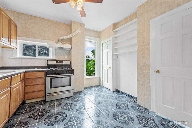 566 Raymond St, Elgin, IL 60120 - kitchen with gas stove, a ceiling fan, under cabinet range hood, dark countertops, and brown cabinetry