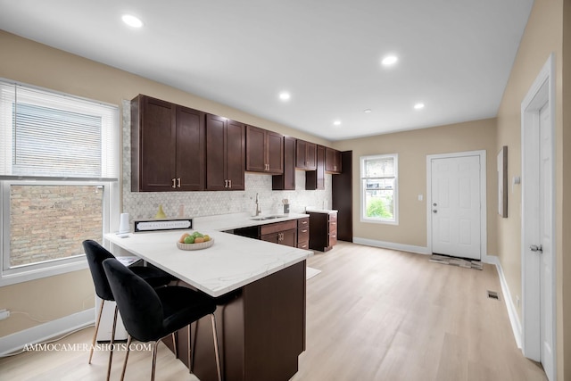 5029 W Superior St, Chicago, IL 60644 - kitchen featuring dark brown cabinetry, light wood-style flooring, a kitchen bar, decorative backsplash, and a peninsula